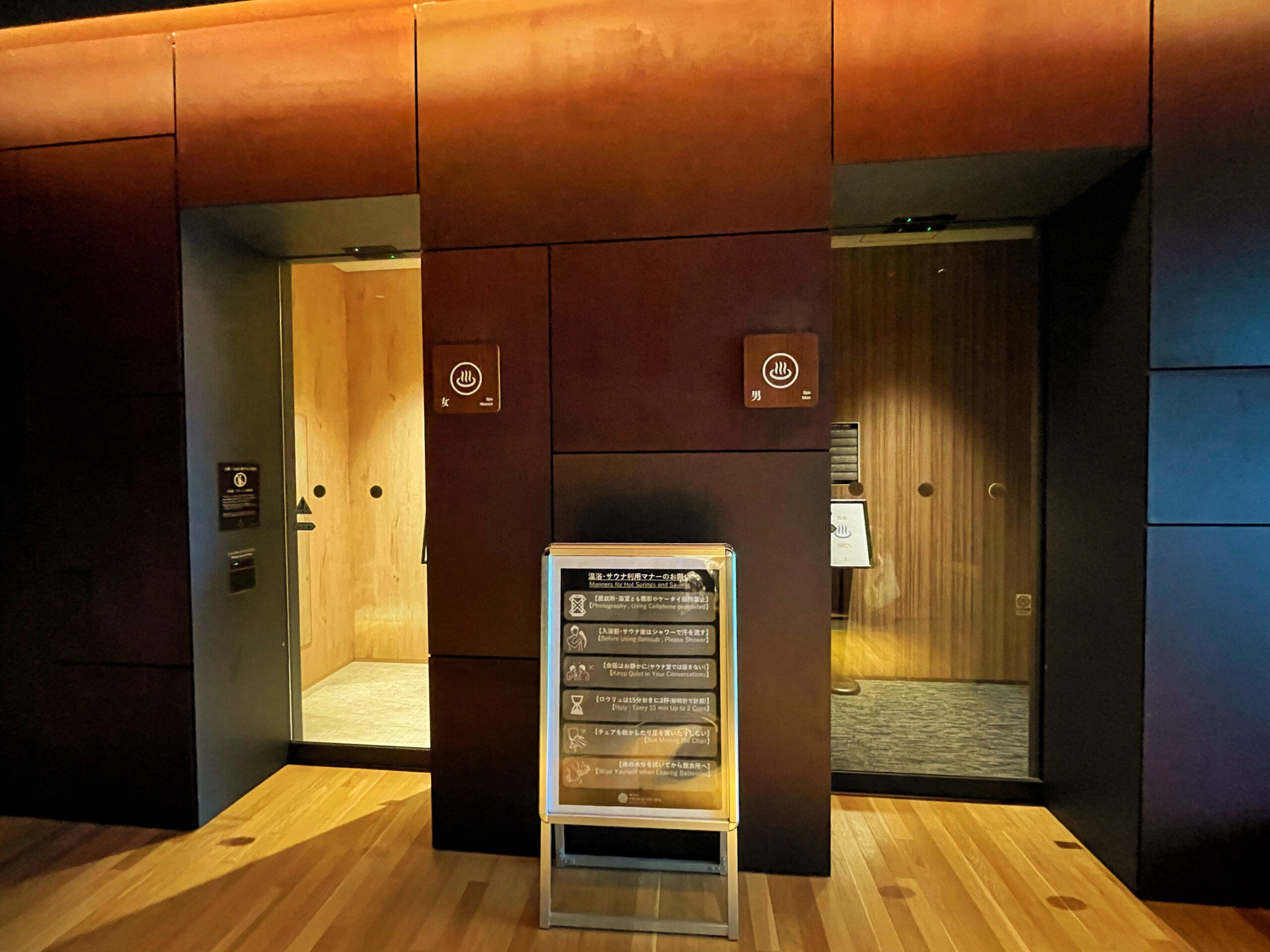 Snow Peak FIELD SUITE SPA HEADQUARTERSの浴場入口｜錆色の壁に男女の温泉マークとマナー看板が並ぶ洗練されたアプローチ｜新潟県三条市
