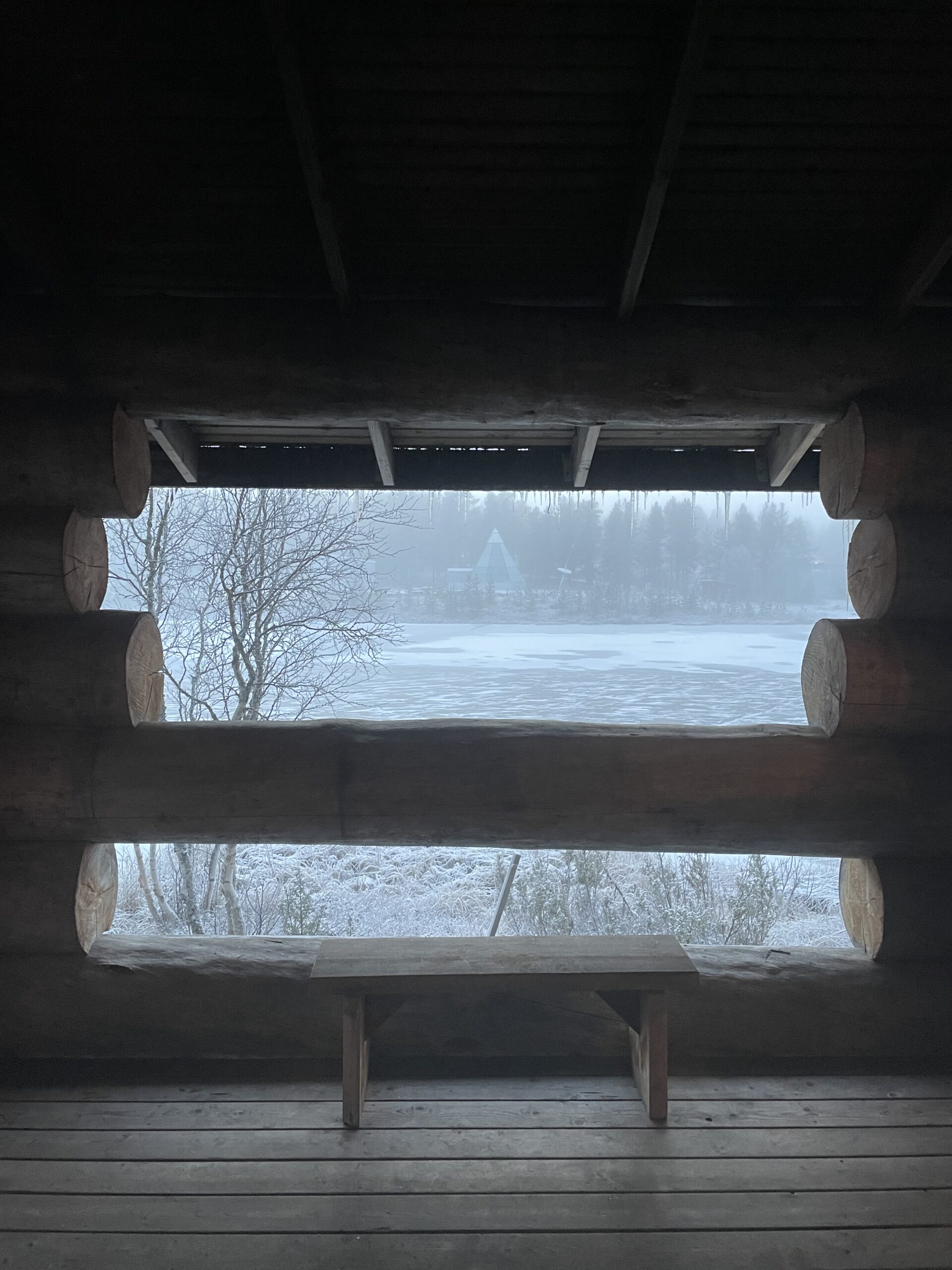 Kakslauttanen Arctic Resort休憩スペースの窓｜丸太の窓枠越しに見える凍結した湖｜Saariselkä