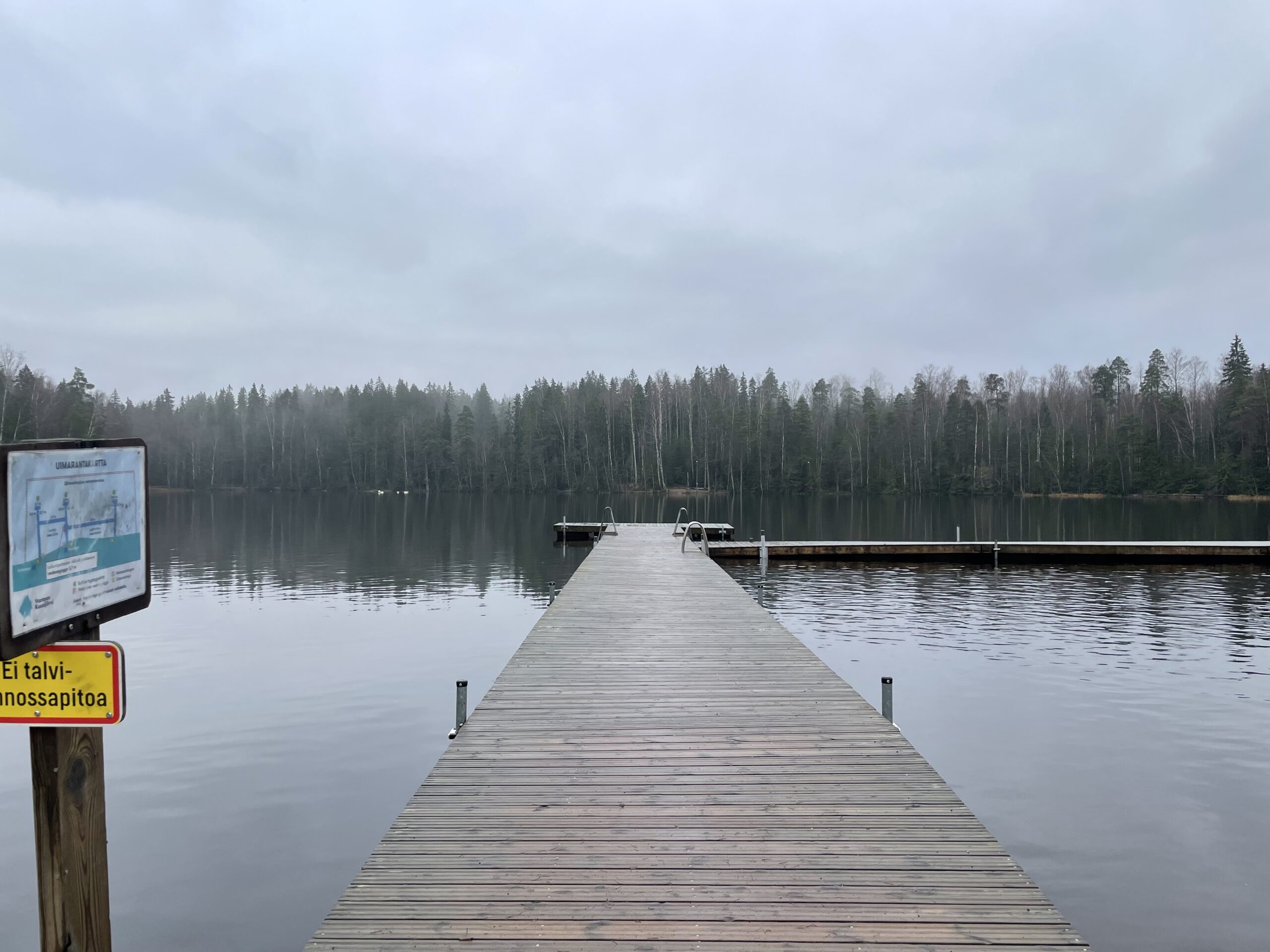 Kuusijärvi湖の木製桟橋｜静かな湖面に森の木々が映り込む曇り空の日、シンプルな木製構造の桟橋｜ヴァンター市・フィンランド