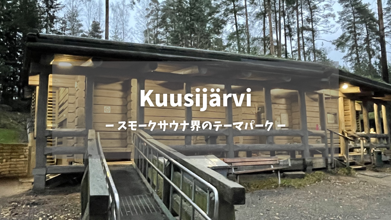 Kuusijärvi（クーシャルヴィ）大型スモークサウナ棟｜温かい照明が灯る丸太造りの木製建築、手すり付きスロープと広いベランダ、針葉樹の森に囲まれた夕暮れの雰囲気｜スモークサウナ界のテーマパーク｜ヴァンター市・フィンランド
