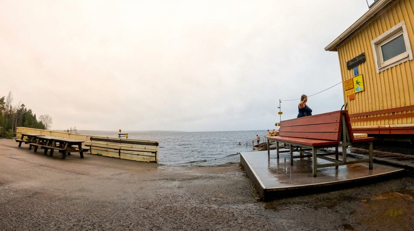 Rauhaniemi Folk Spa外気浴スペース全景｜ナシ湖畔に並ぶ木製長ベンチ、右手に黄色いサウナ施設とウッドデッキ、奥に桟橋と入水階段、曇り空の下の開放的なととのいエリア｜フィンランド・タンペレ