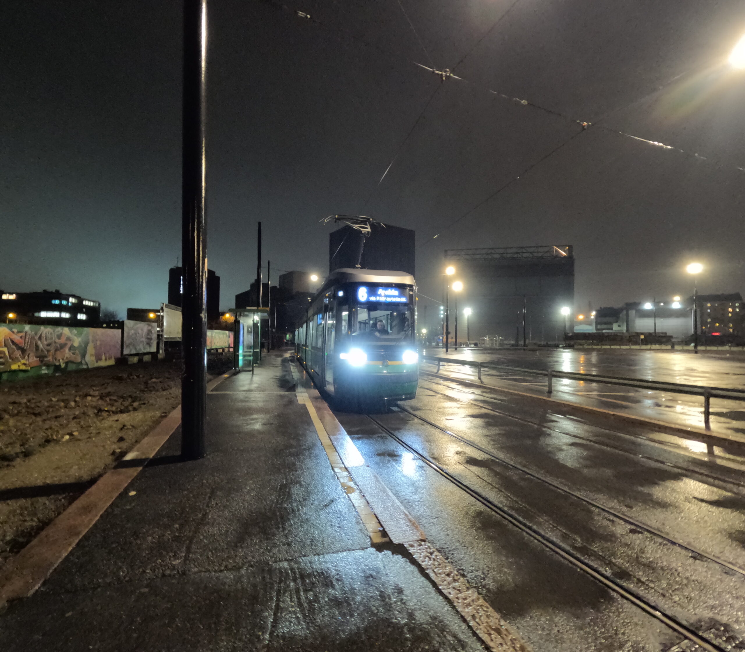 ヘルシンキ市内からlöylyへ向かうトラム（路面電車）｜夜の濡れた路面を走る青いトラム6番線、架線と街灯が照らす雨上がりのヘルシンキの街並み｜フィンランド