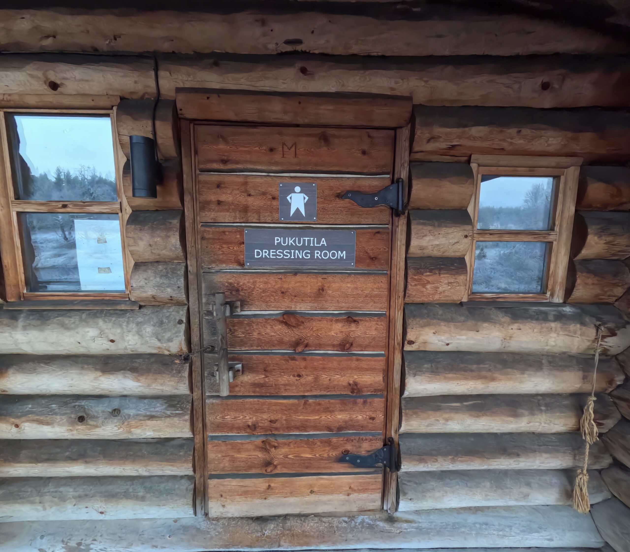 Kiilopää更衣室入口｜丸太造りの木製扉に「PUKUTILA DRESSING ROOM」の看板、左右に小窓がある伝統的なログハウス建築｜フィンランド・サーリセルカ・北極圏