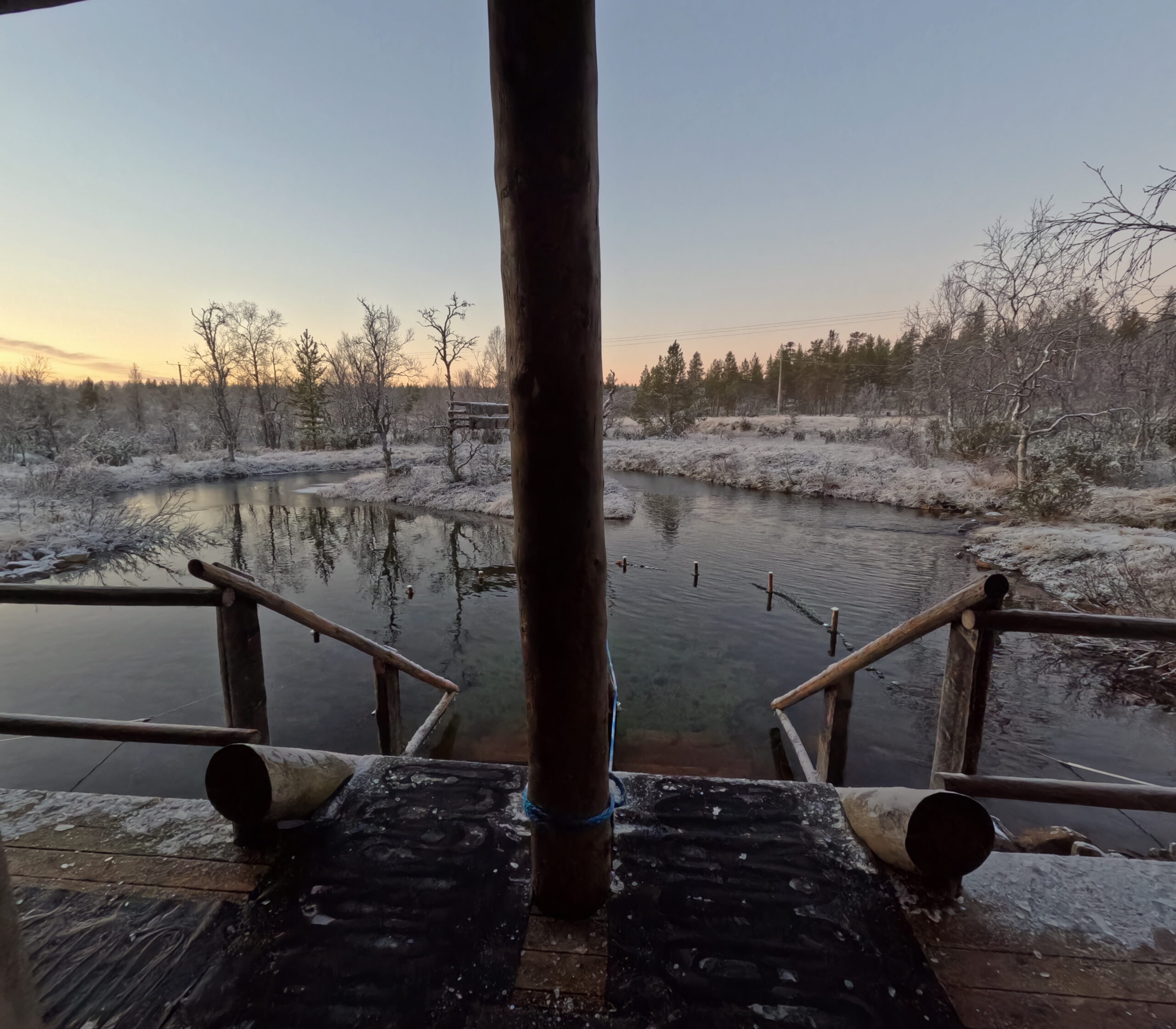Kiilopää小川の水風呂入口｜木製の手すりと階段、霜で白く染まった岸辺、夕焼け空が反射する清流、針葉樹林に囲まれた静寂な空間｜フィンランド・サーリセルカ・北極圏