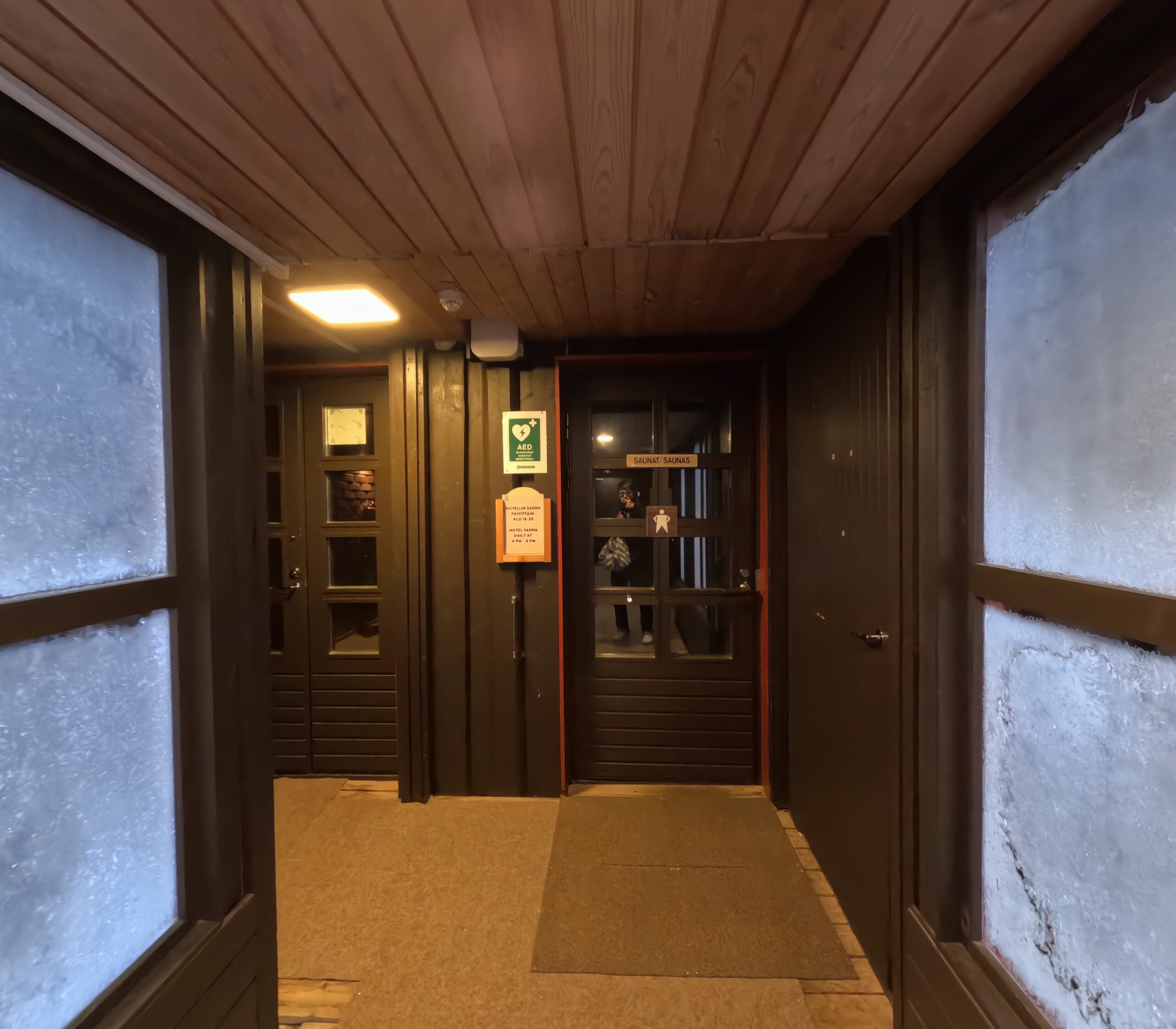 Kiilopääのホテル内通路に設置されたサウナ利用時間案内看板「毎日16時~20時」と記載｜木製ドアとフィンランド語・英語の併記｜フィンランド・ラップランド地方