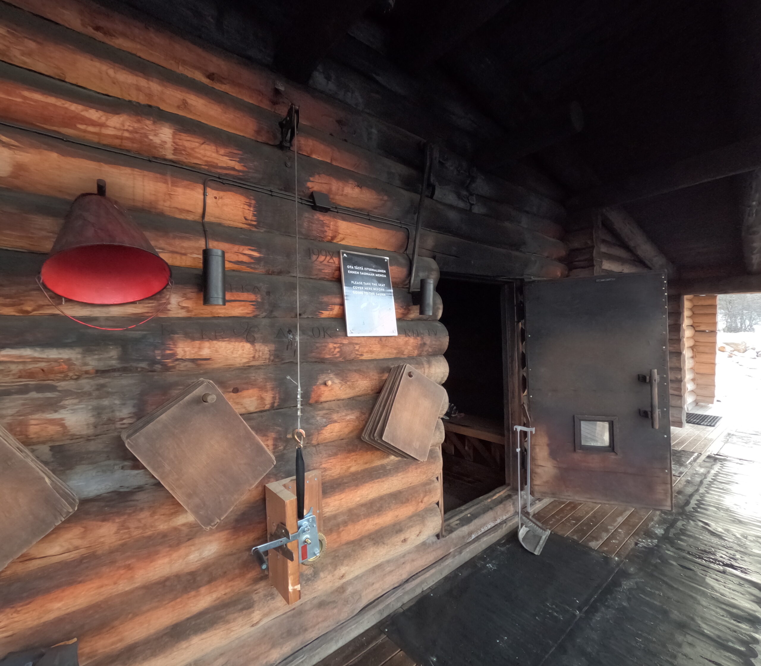 Kiilopääサウナマット置き場｜丸太造りの外壁に吊るされた木製サウナマット、赤い消火器、「PLEASE TAKE THE SEAT COVER」の案内看板｜フィンランド・サーリセルカ・北極圏