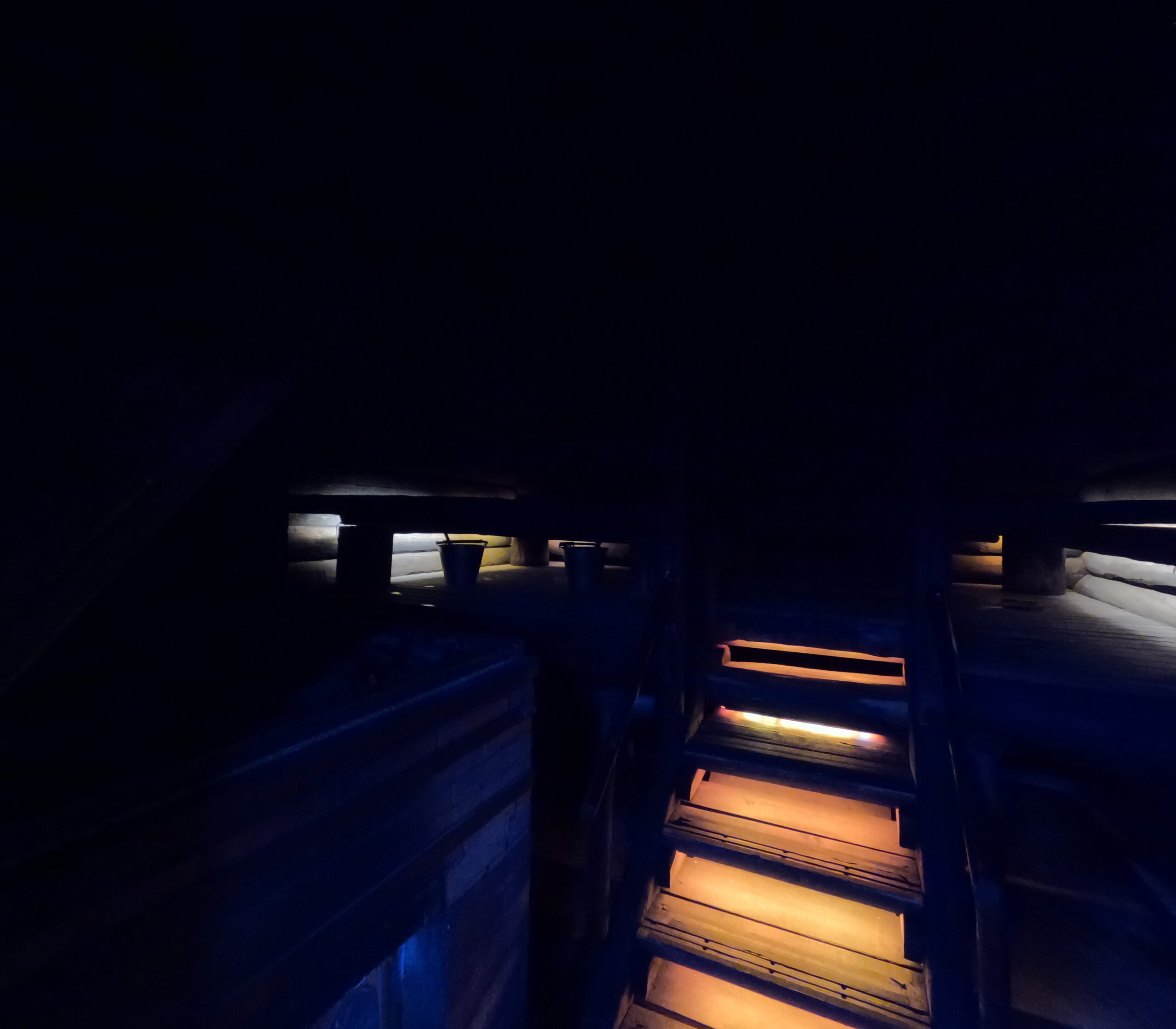 Kiilopääスモークサウナ室内への階段｜温かいオレンジ色の照明が照らす木製階段、薄暗い空間に青い光が差し込む神秘的な雰囲気｜フィンランド・サーリセルカ・北極圏