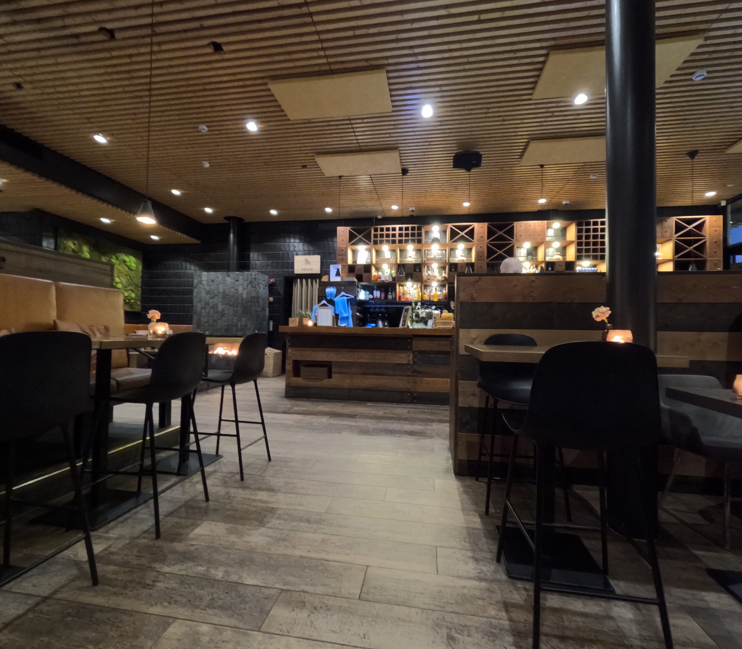 Kuuma休憩ラウンジ｜木製天井とタイル床、黒いカウンターチェア、ハイテーブル、壁面にサウナグッズ展示、間接照明、シックなインテリア｜フィンランド・タンペレ
