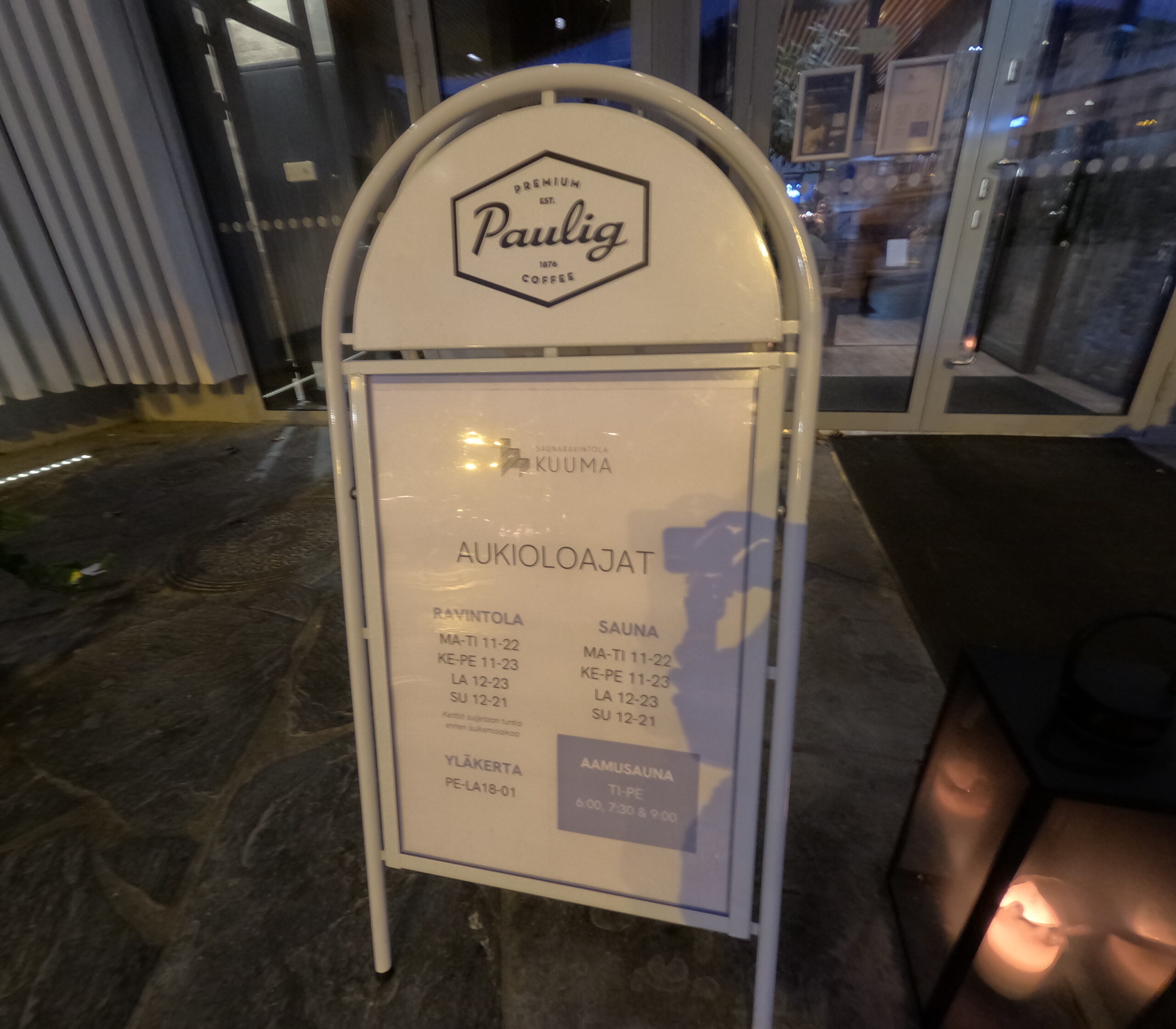 Kuuma営業時間案内看板｜Pauligブランドの白い看板、レストランとサウナの営業時間表示、フィンランド語と英語併記｜タンペレ