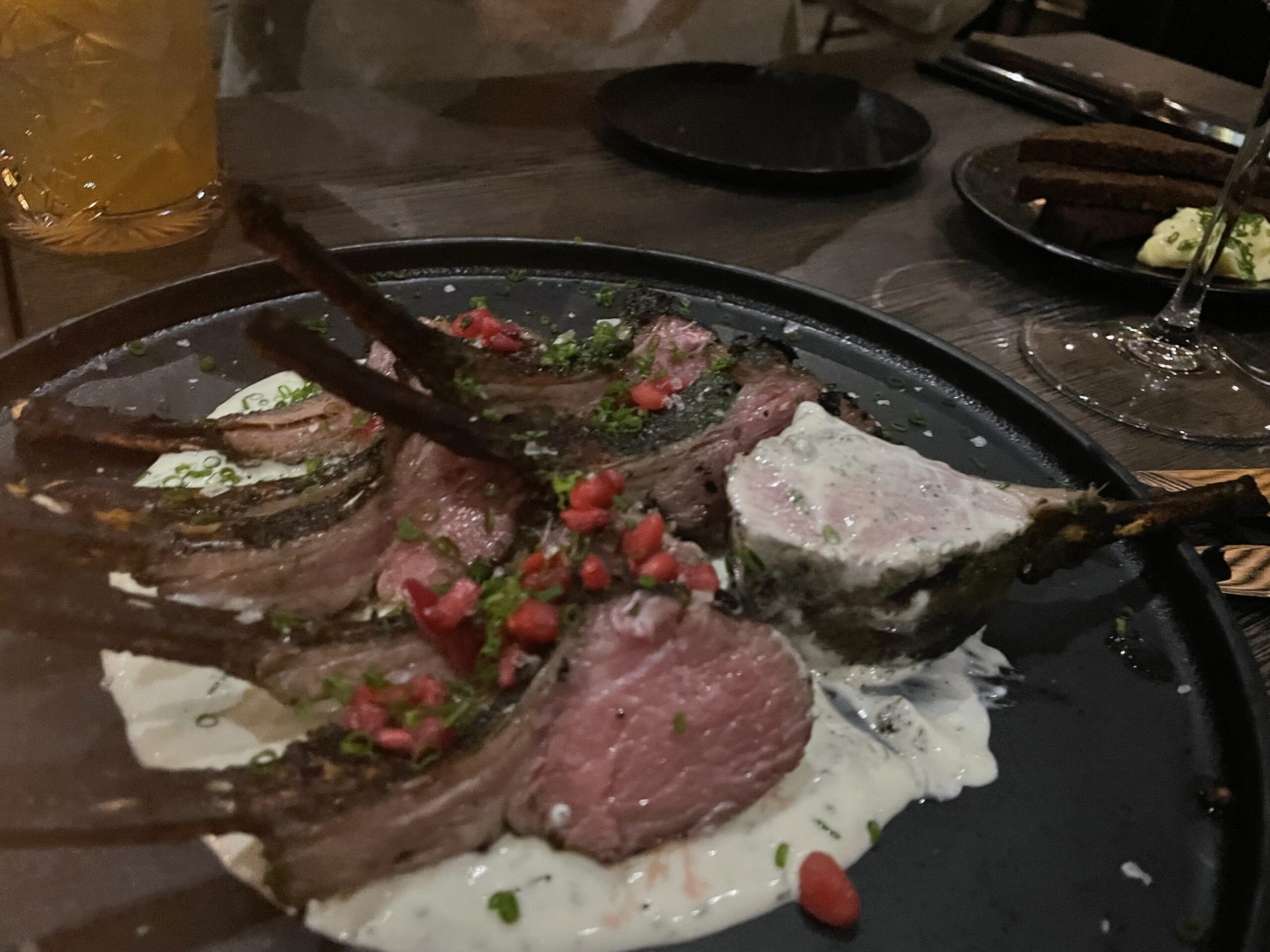 Kuumaレストラン料理｜黒いプレートに盛られた薄切り肉のカルパッチョ風、ハーブとピンクペッパー添え、北欧ガストロノミー、サウナ後の食事｜タンペレ