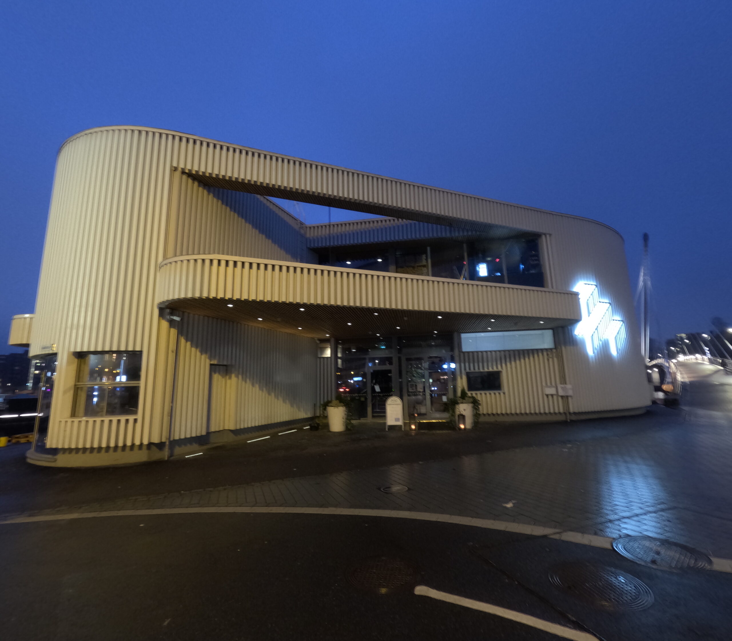 Kuuma夜景全景｜タンメルコスキ川に浮かぶ白いモダン建築、対岸のタンペレ市街地夜景、吊り橋、川面に映る光、曇り空｜フィンランド・タンペレ