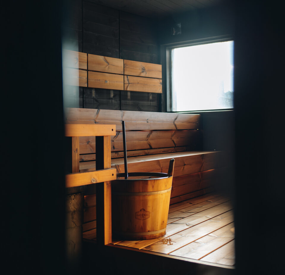 Kuumaスモークサウナ室内｜木桶とバケツが置かれた木製座面、暗めの照明、窓からの自然光が差し込む雰囲気、伝統的なフィンランドサウナ空間｜タンペレ