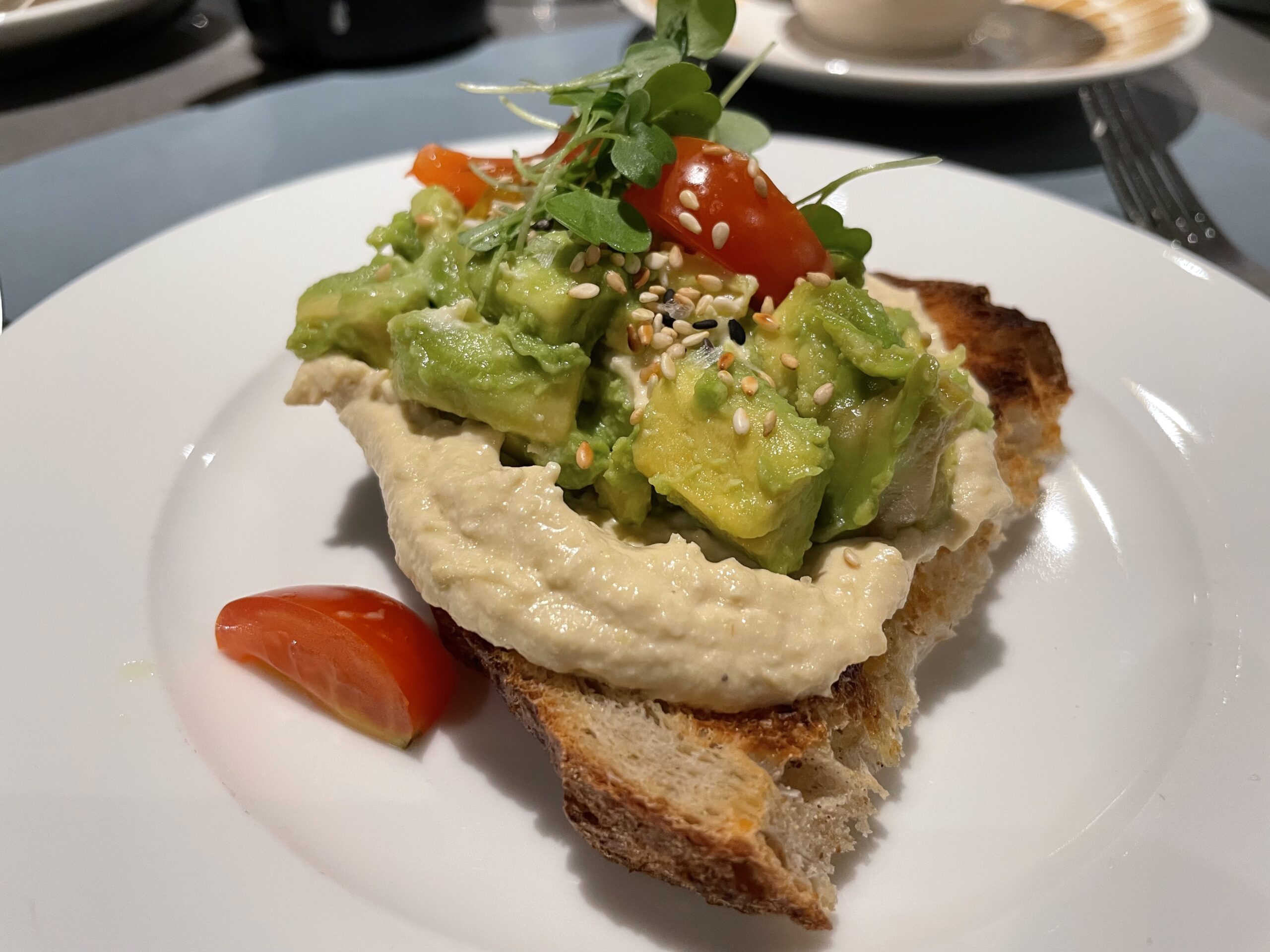 NH Collection Helsinki Grand Hansa朝食料理のプレート｜トーストにフムス・アボカド・チェリートマト・ゴマをトッピング、白い皿に美しく盛り付けられた健康的でカラフルな一皿｜ヘルシンキ中央駅前・フィンランド