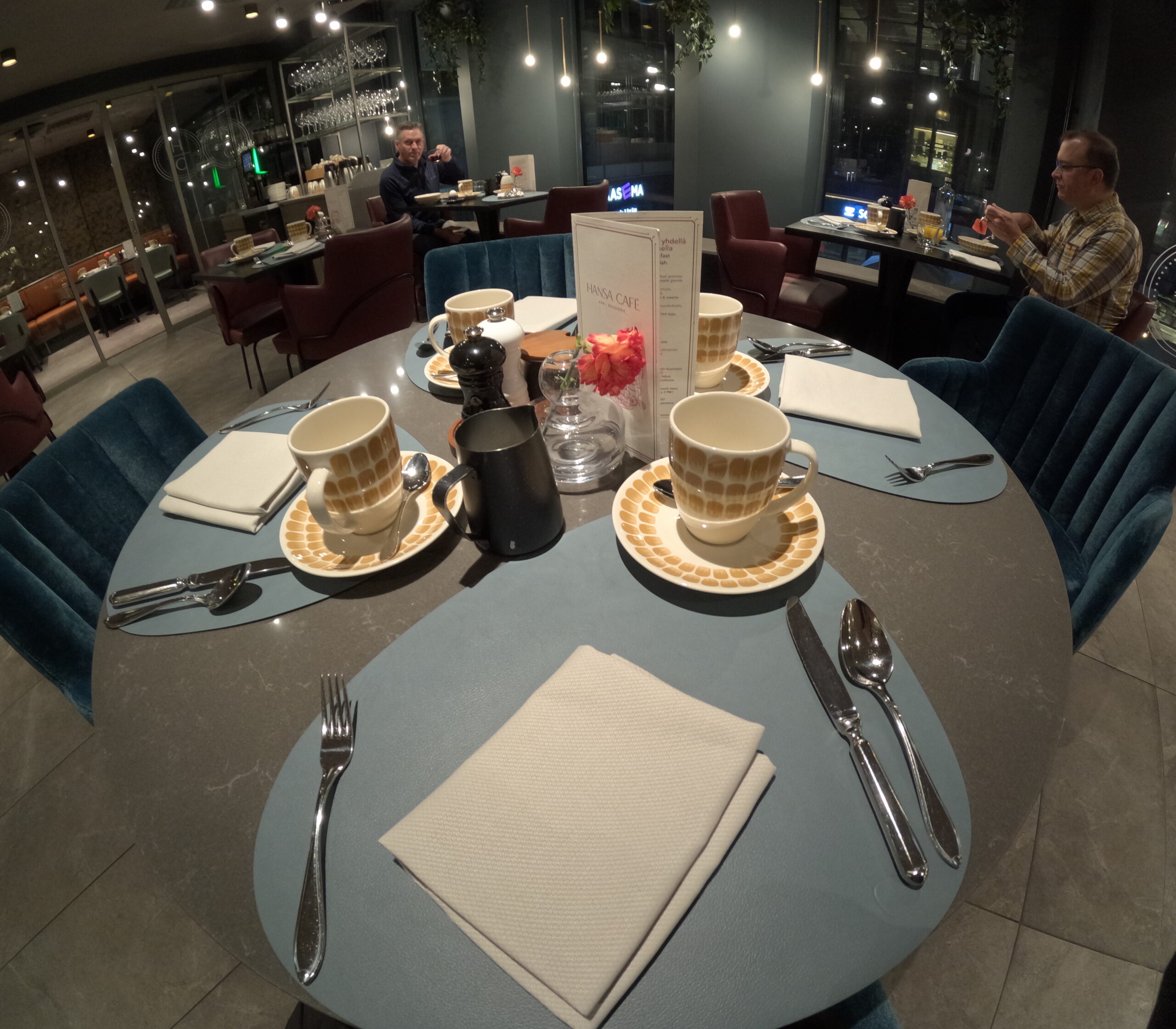 NH Collection Helsinki Grand Hansa朝食レストラン内部｜ブルーベロアの椅子と洗練されたテーブルセッティング、モダンな照明とパターン入りカップが並ぶエレガントな空間｜ヘルシンキ中央駅前・フィンランド