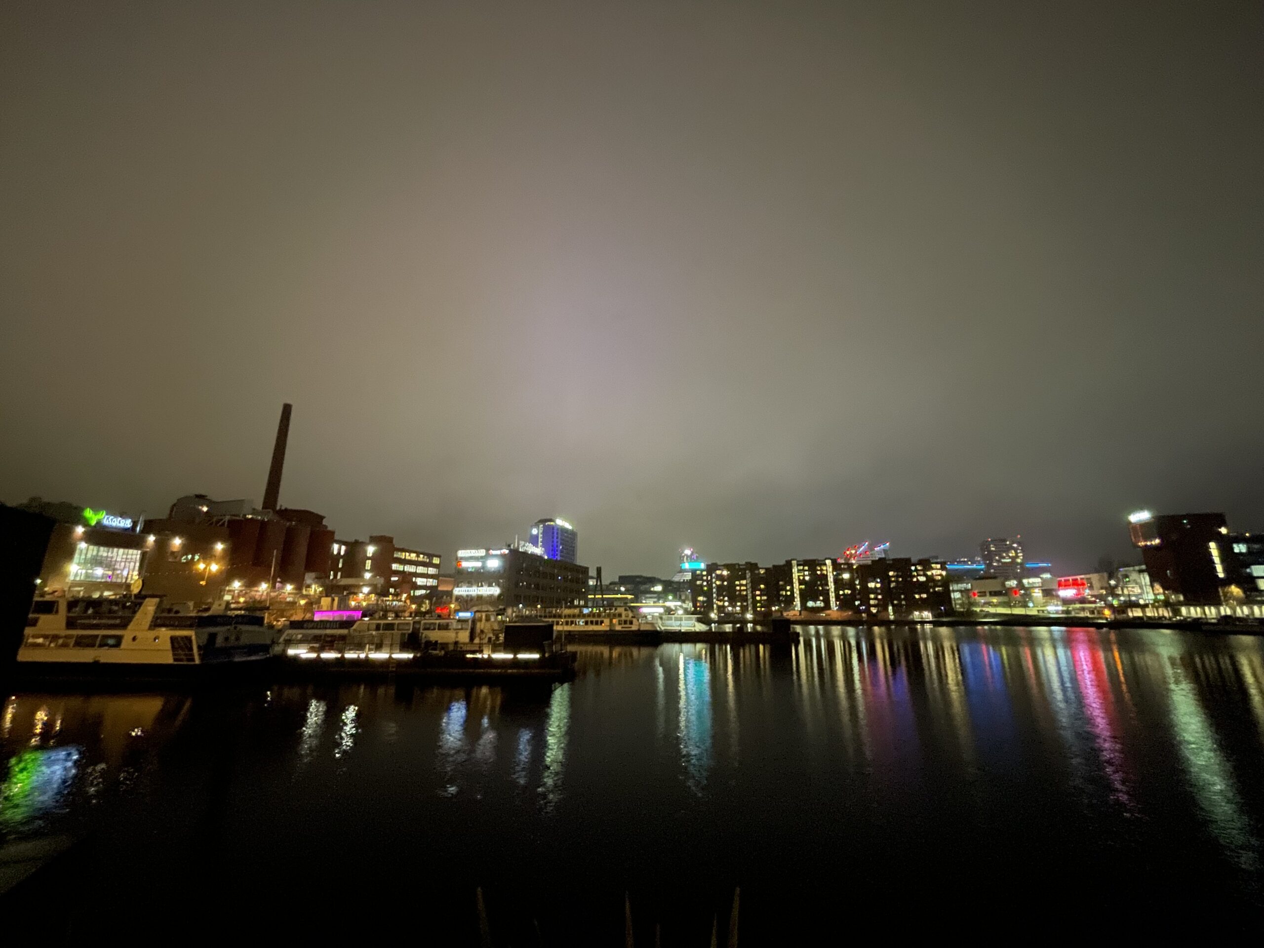 タンペレ市街地夜景｜タンメルコスキ川対岸から見たカラフルな建物群、川面に映る光、工場の煙突、曇り空｜フィンランド・タンペレ